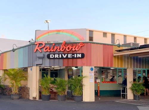 Colorful exterior of Rainbow Drive-In with a rainbow mural, featuring palm trees and a welcoming entrance.