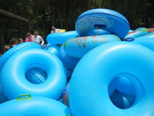 A pile of blue inflatable tubes stacked together, with people in the background preparing for a water activity.