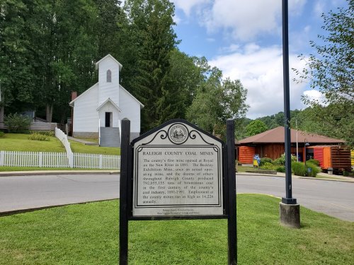 Historical marker about Raleigh County coal mines, with a white church and trees in the background.