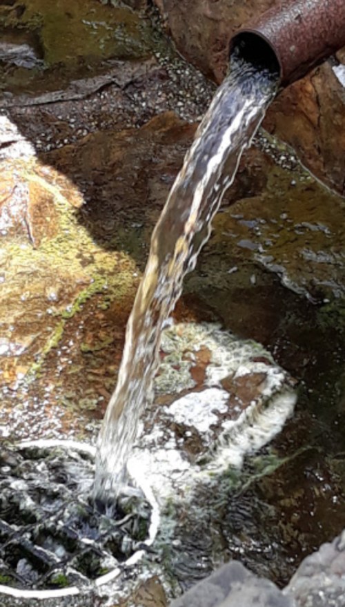 Water flowing from a pipe into a rocky surface, creating ripples in a small pool.