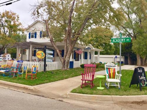A colorful house with rocking chairs on the porch, located at the corner of Academy Ave, surrounded by trees.