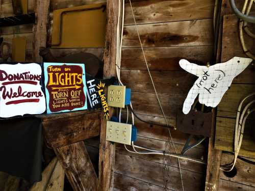 A rustic wooden wall with signs for donations and instructions to turn off lights, featuring a hand pointing.