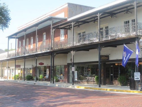 Historic buildings with balconies line a brick-paved street, featuring shops and decorative flags.