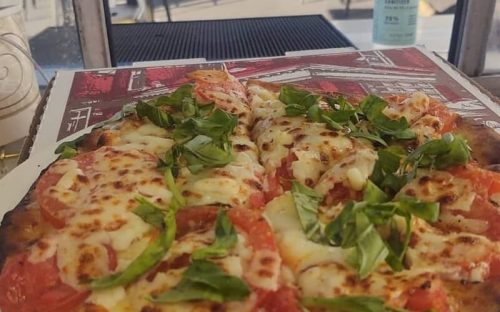 A close-up of a pizza topped with melted cheese, fresh tomatoes, and basil, served in a takeout box.