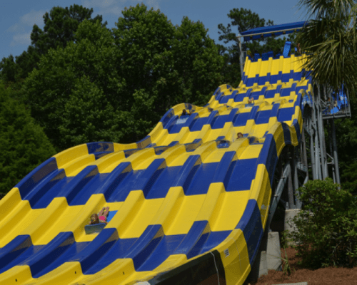 A colorful water slide with yellow and blue patterns, surrounded by trees and clear blue skies.