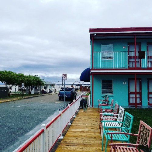 Colorful motel with turquoise and red accents, lined with pastel chairs, under a cloudy sky.