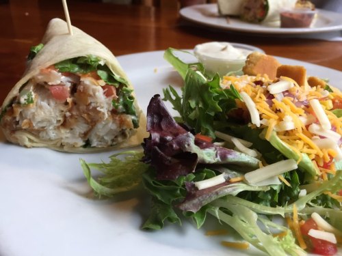 A plate featuring a chicken wrap with lettuce and tomato, alongside a fresh salad topped with cheese and dressing.