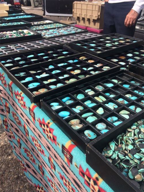 A table covered with trays of turquoise stones, set against a colorful patterned fabric.
