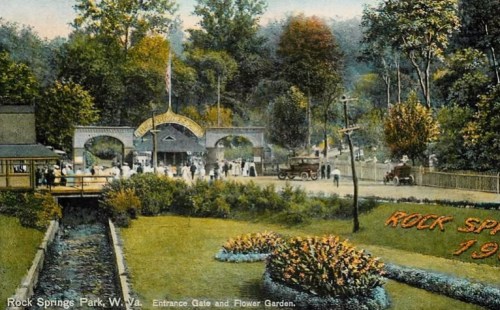 Historic view of Rock Springs Park entrance with flower garden, people, and vintage cars, circa 1910.