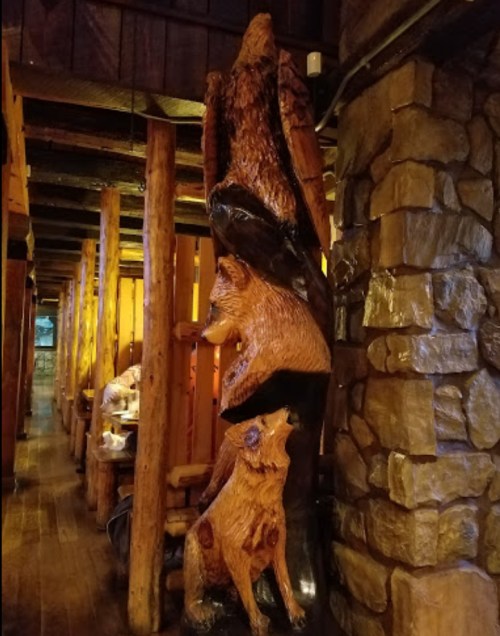 Wooden sculpture of a bear and two wolves, set in a rustic interior with wooden beams and stone walls.