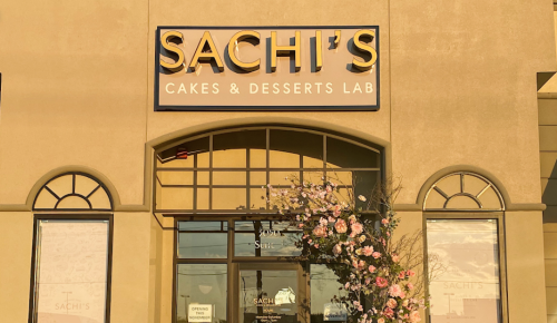 Exterior of Sachi's Cakes & Desserts Lab, featuring a sign and floral decoration by the entrance.