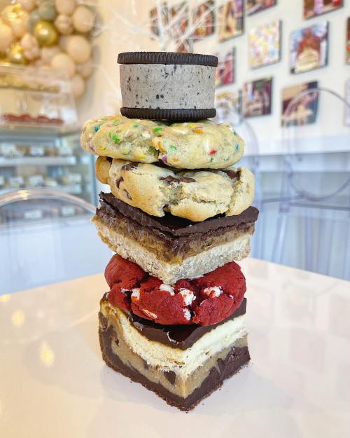 A towering stack of colorful cookies and layered desserts, including a cookie on top, set against a bright background.
