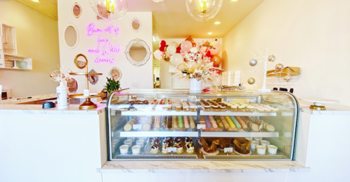 A bright dessert shop display featuring a glass case filled with colorful pastries and a decorative backdrop of balloons.