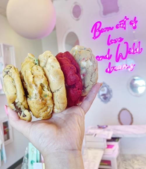 A hand holding four colorful cookies in front of a neon sign that says "Born out of love and wild dreams."