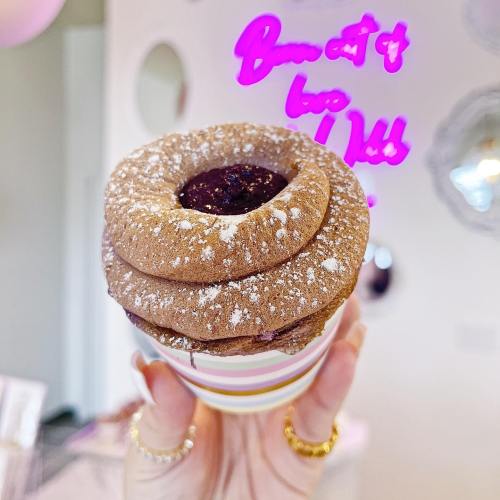 A hand holding a layered chocolate dessert topped with powdered sugar and a berry filling, with a neon sign in the background.