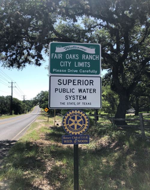 Welcome sign for Fair Oaks Ranch city limits, featuring public water system information and a Rotary Club emblem.
