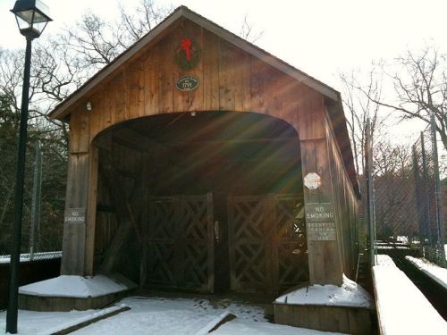 A wooden structure with a festive wreath, featuring double doors and signs, surrounded by snow and trees.