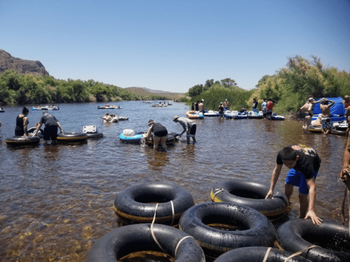 People enjoying a sunny day by a river, floating on inner tubes and wading in shallow water.