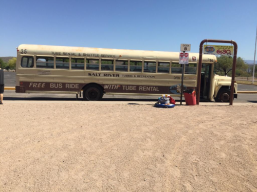 A vintage bus labeled "Salt River Tube Rental" parked near a sandy area, with a sign for free bus rides.