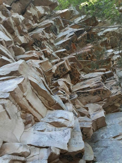 A close-up view of a rocky cliff face with large, uneven stone formations and patches of greenery above.