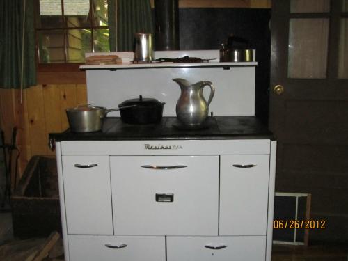 A vintage white kitchen stove with pots, a kettle, and a pitcher on top, set in a rustic wooden room.