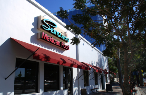 Exterior of Serrano's Mexican Food restaurant, featuring a colorful sign and awnings, with a modern building in the background.