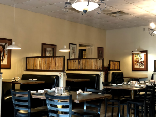 A cozy restaurant interior with wooden tables, black chairs, and framed artwork on the walls. Soft lighting creates a warm atmosphere.