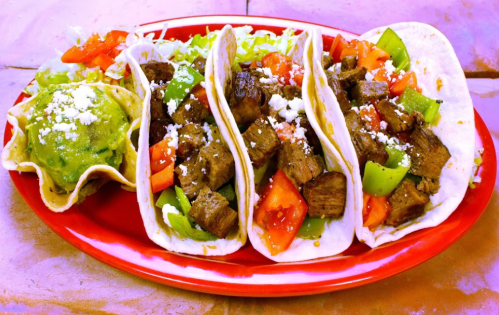 A vibrant plate of three beef tacos with tomatoes and peppers, served with a side of guacamole.
