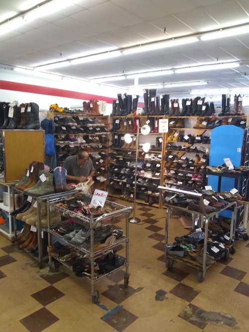A shoe store with shelves of various boots and shoes, and a person sitting at a table in the center.