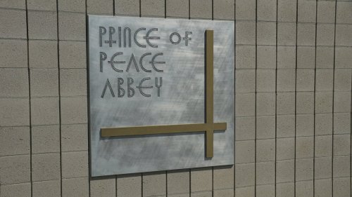 Sign for Prince of Peace Abbey, featuring stylized text and a cross design on a textured wall.
