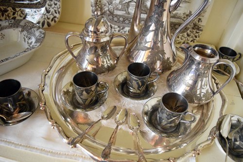 A silver tea set with intricate leaf designs, including cups, a teapot, and a serving tray, displayed elegantly.