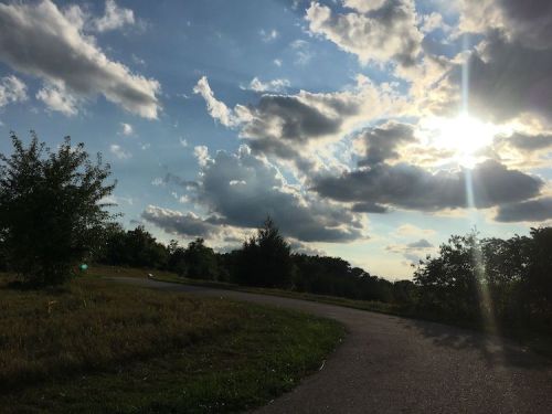 A winding path through a grassy area under a bright sky filled with clouds and sunlight.