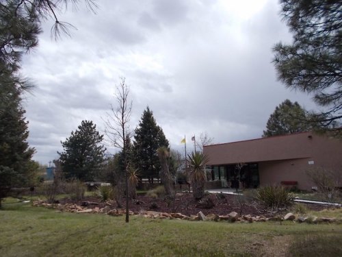A cloudy sky over a landscaped area with trees and shrubs, featuring a building in the background.