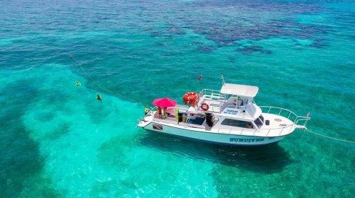 A boat with a red umbrella is anchored in clear turquoise waters, with snorkelers exploring nearby.