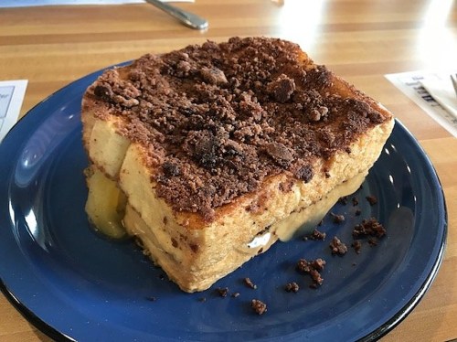 A slice of baked French toast topped with a crumbly brown sugar topping, served on a blue plate.