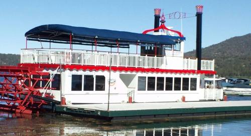A colorful paddleboat docked at a lakeside, featuring a blue canopy and red accents against a mountainous backdrop.
