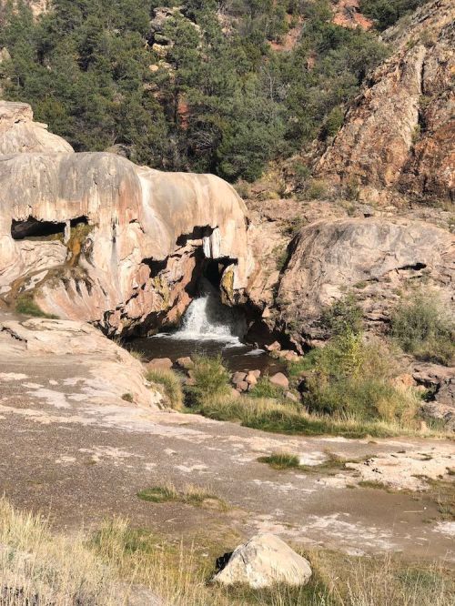 A rocky landscape with a small waterfall flowing into a pool, surrounded by greenery and rugged terrain.