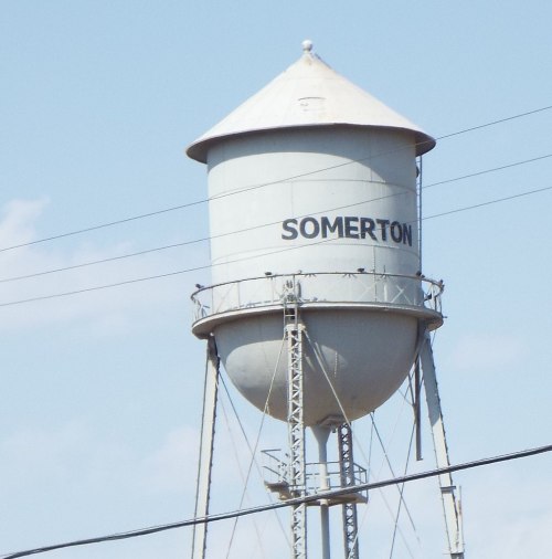 A tall water tower with the word "SOMERTON" painted on it, set against a clear blue sky.