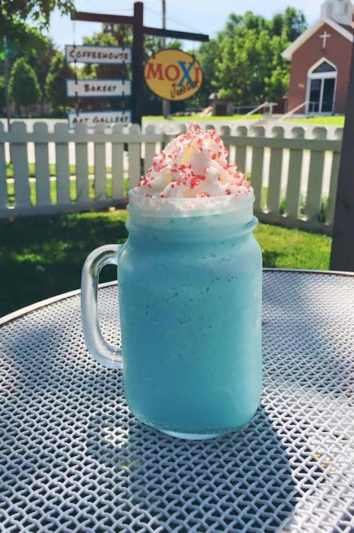 A blue milkshake topped with whipped cream and red sprinkles, served in a mason jar on a table outdoors.