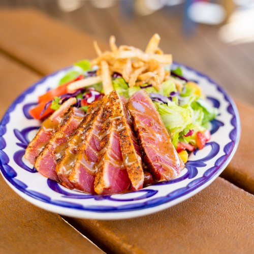 A plate of sliced grilled tuna served with a fresh salad and crispy onions on top.