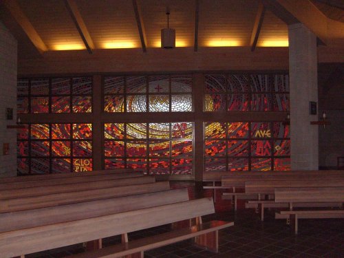Stained glass window depicting a vibrant, swirling design in warm colors, viewed from inside a church.