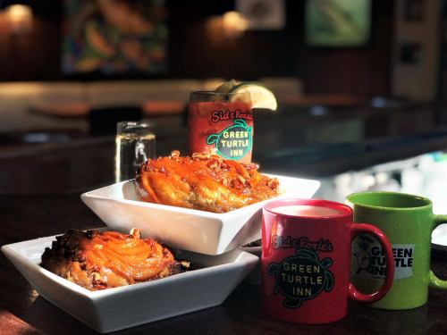 Two dishes of food topped with orange sauce, alongside colorful mugs and a drink, set in a cozy restaurant.