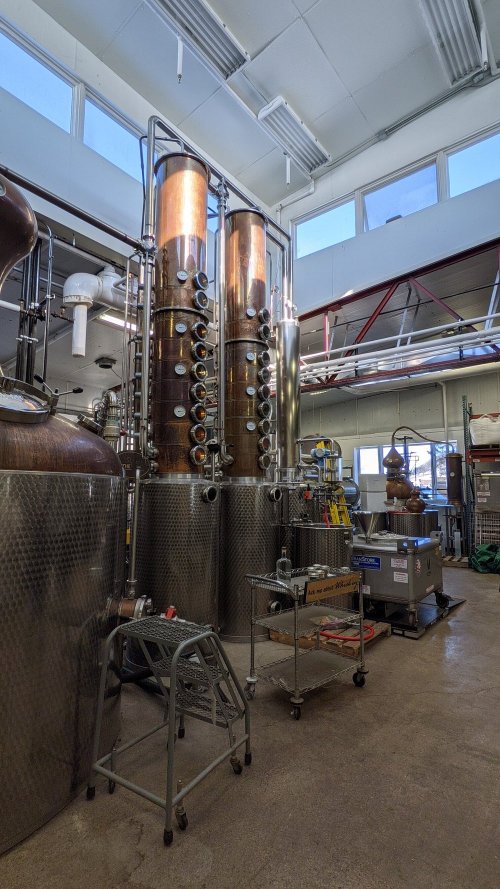 A distillery interior featuring tall copper stills, metal equipment, and a bright, spacious workspace.