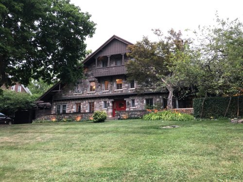 A large stone house with a steep roof, surrounded by greenery and a well-maintained lawn.