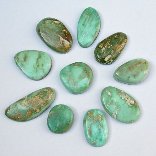 A collection of smooth, polished green stones arranged in a circular pattern on a light background.