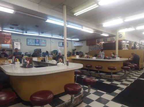 A retro diner interior with a counter, red stools, and patrons enjoying meals in a casual atmosphere.