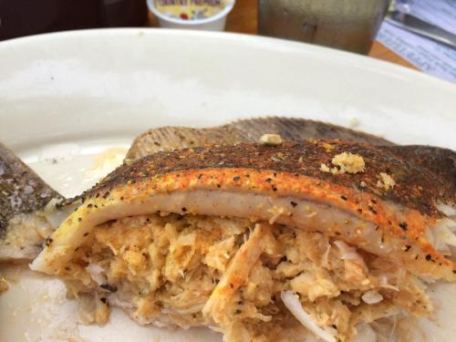 A plate with a baked fish fillet, stuffed with a golden-brown crab meat filling, garnished with spices.