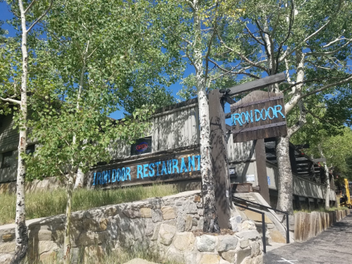 Exterior of Iron Door Restaurant, featuring a wooden sign and surrounded by trees under a clear blue sky.