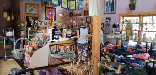 A colorful shop filled with crafts, clothing, and decorations, featuring a customer browsing at the counter.