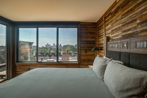 Cozy bedroom with wooden walls and a large window showcasing a city skyline view.